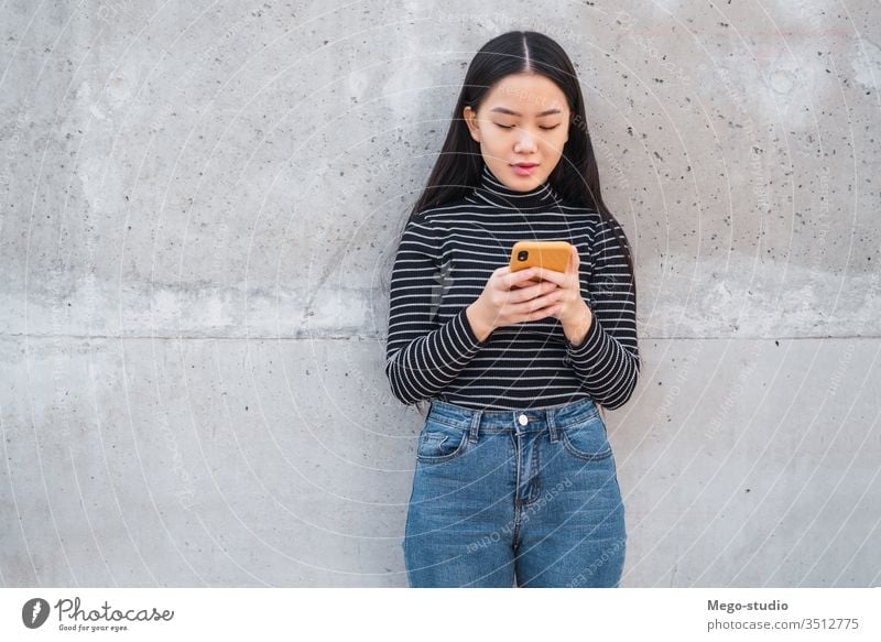 Asian woman using her mobile phone. grey wall asian japanese chinese girl korean cellphone telephone female smart young smartphone lady text people use message