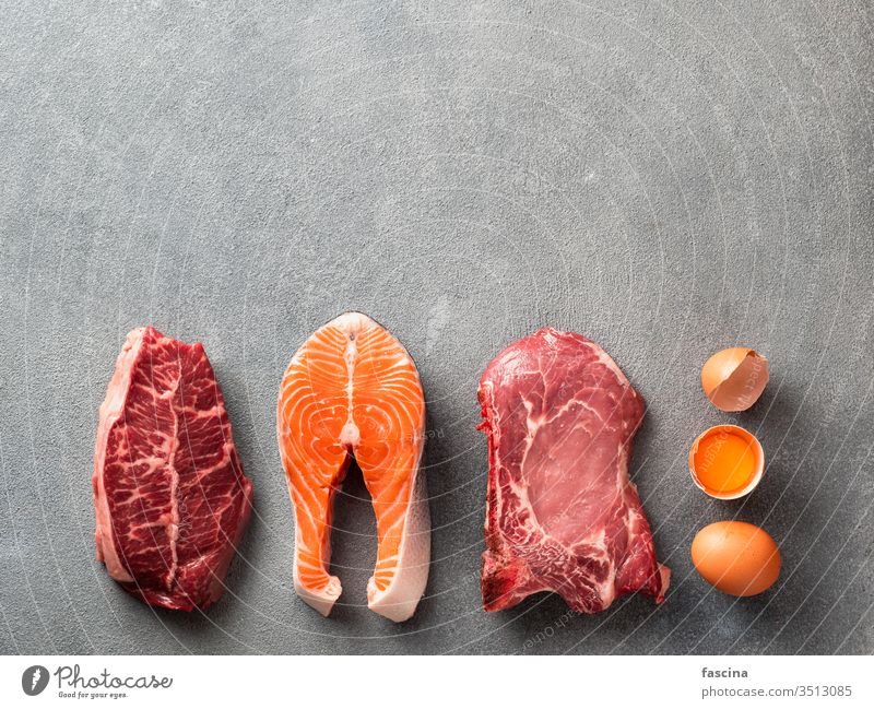 Carnivore or keto diet, zero or low carb concept, top view carnivore paleo lay flat steak beef pork rib eye eggs gray stone background fish meat ingredients raw