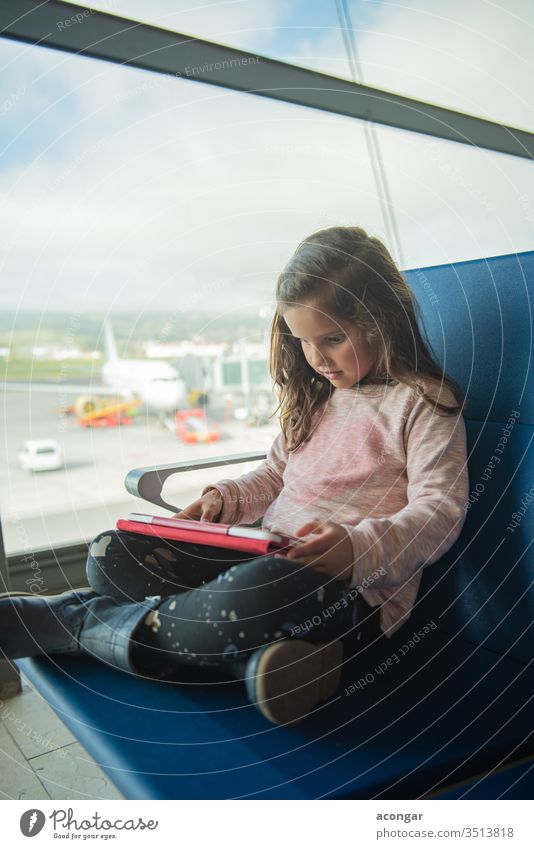 Little cute girl waiting for plane at airport terminal, using digital tablet Child adorable aircraft airline caucasian chair childhood computer delay departure