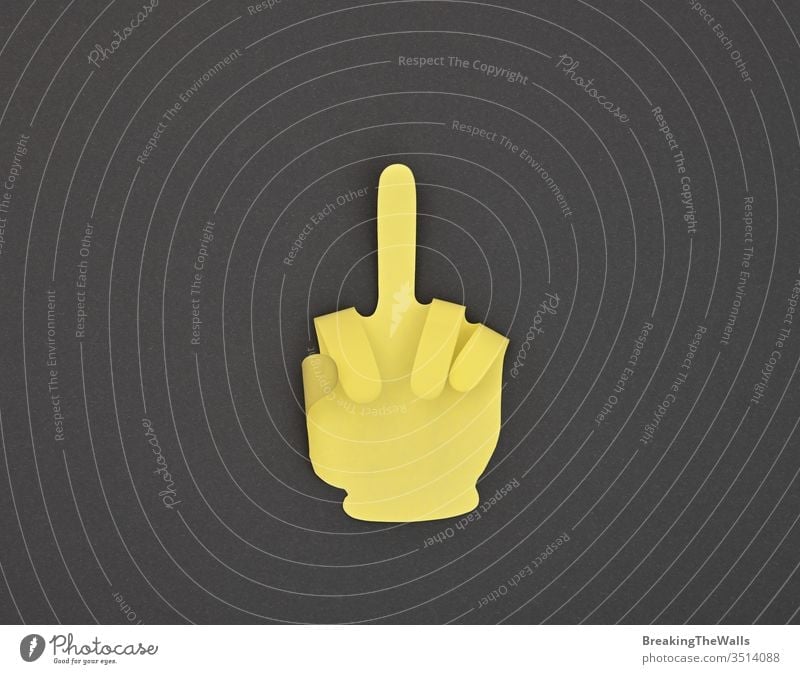 Paper made finger rude gesture sticker on grey one middle insult offensive hand shape paper yellow closeup note black background dark business metaphor concept