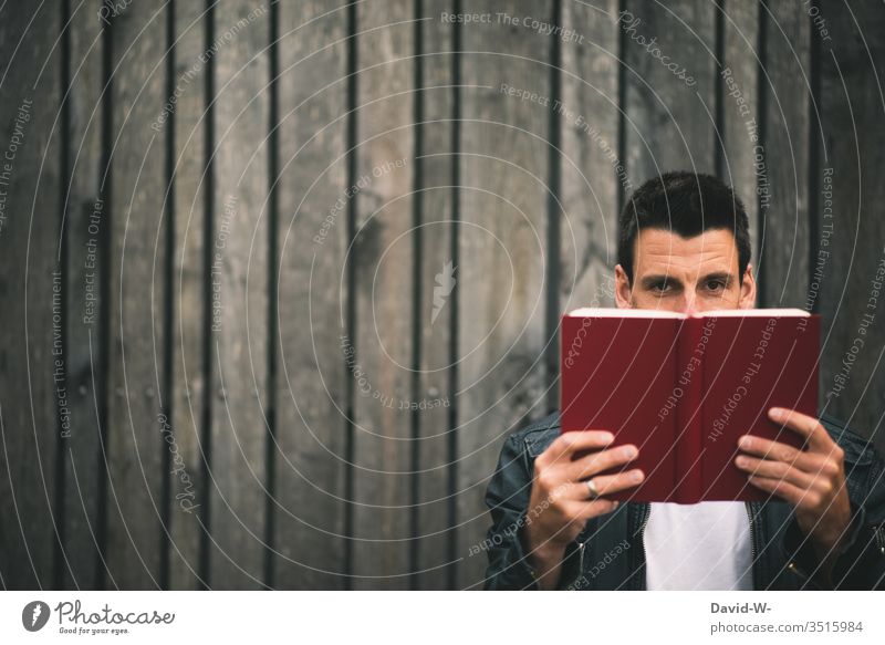 Man holds a book in his hands in front of a wooden wall and looks into the camera Book Wooden wall Reading Education educated Study Reading matter Page Reader