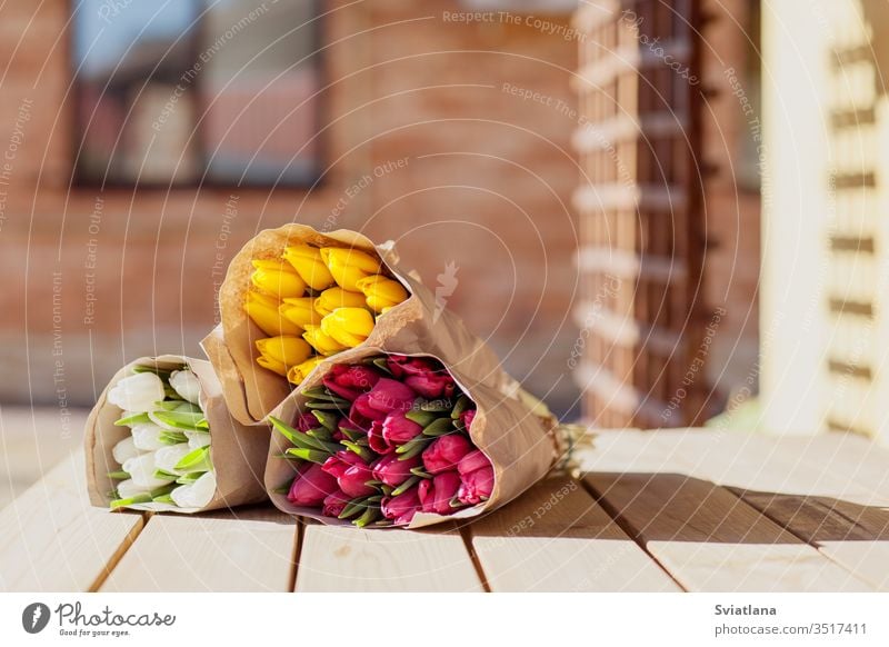 Beautiful colorful bouquets of tulips in craft paper lie on the street on a wooden table. Side view market flower spring red pink march decoration floral green