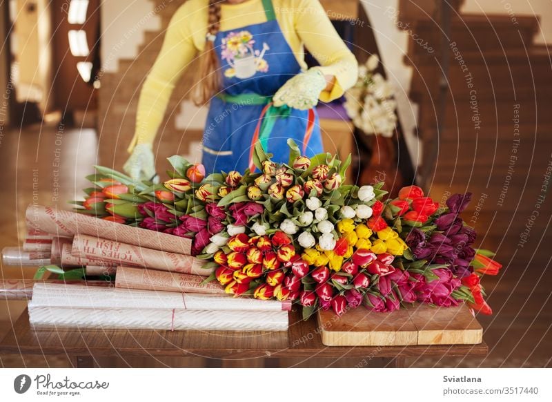 Girl florist is packing beautiful tulips in a flower shop in kraft paper. Women's Day and Valentine's Day bouquet hands view pink packaging girl woman