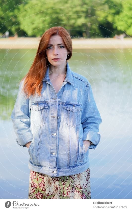 authentic young woman wearing denim jacket over summer dress standing by  lake - a Royalty Free Stock Photo from Photocase