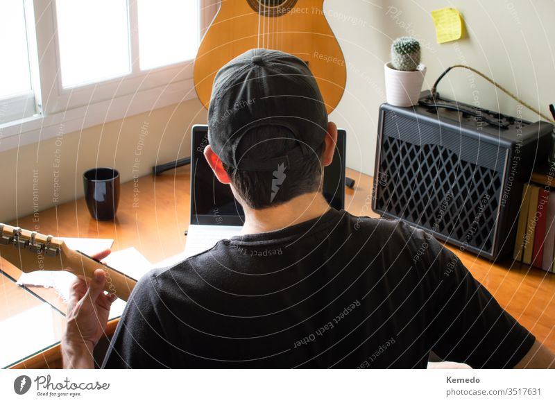 Young musician in cap learning to play the guitar using a computer at home. Concept of learning music with online classes, using technology. laptop practice man