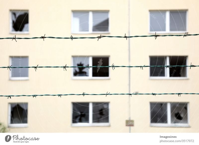 Rows of barbed wire in the background an abandoned residential building with broken windows. Concept of ghost town, isolation and security. prison, refugee, loneliness