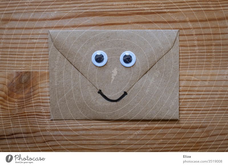 A friendly envelope with wagging eyes and a smiling face on wood Envelope (Mail) kind Face peer wobbly eyes Funny nice Letter (Mail) enjoyable communication