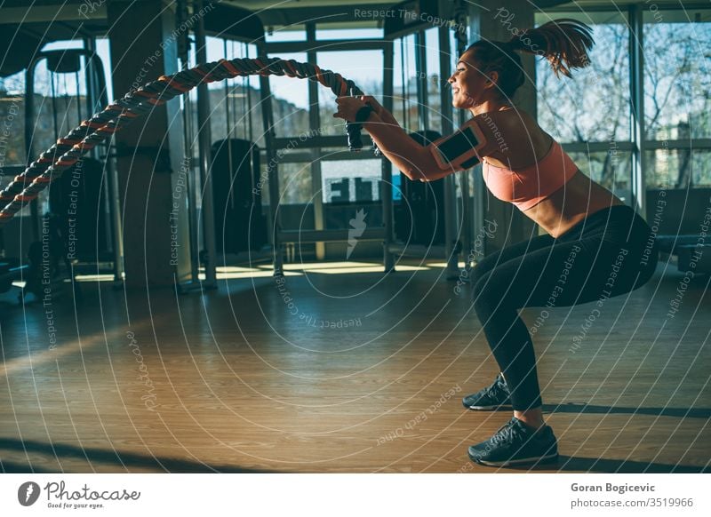 Battle rope, fitness and woman in studio for exercise, strength training  and cardio workout burning calories. Wellness, focus and healthy girl in a  squat pose moving ropes with a blue background Stock