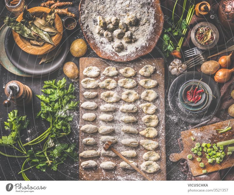 Homemade gnocchi making preparation. Potatoes dough on dark rustic kitchen table with cutting board and healthy ingredients. Tasty home cuisine. Top view. Still life