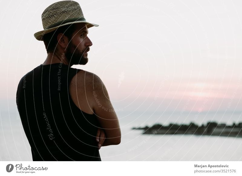 Young man enjoying sunset by the sea adult adventure alone beach coast dawn dusk enjoyment evening freedom guy handsome hat holiday horizon landscape leisure