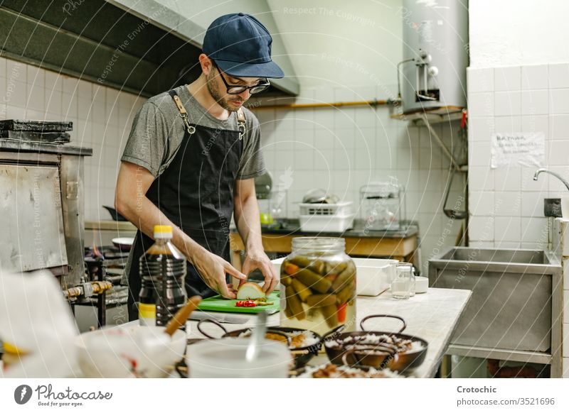 Man with glasses and a cap cooking in a restaurant kitchen with pots of food, oil and pans commercial containers elements professional stainless appliances