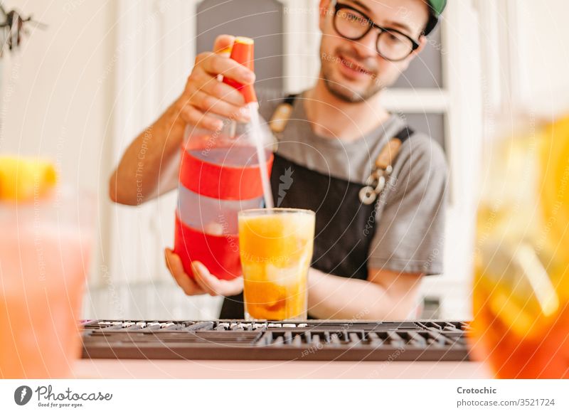 Waiter with apron, glasses and cap throwing soda into a glass with a cocktail at a bar splash mix bottle dispensed pouring ice waiter hotel fresh alcohol