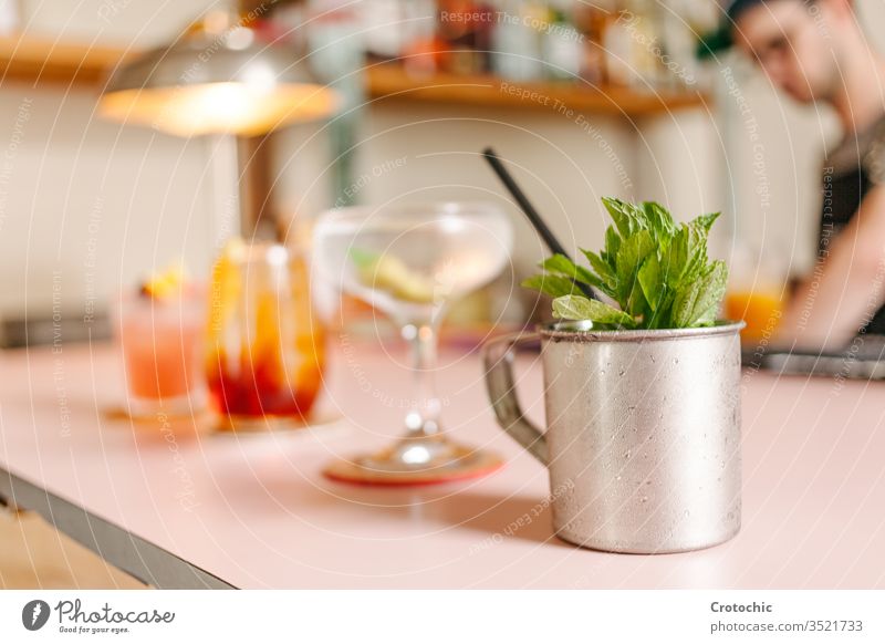 Selective focus on a metal cup with mint and three cocktail glasses prepared next to it on a bar metallic recipient set raw variety selective serve ready