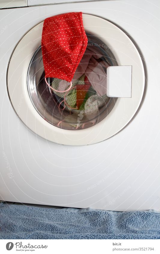 Red self-sewn protective mask made of fabric with dots, hangs before washing, disinfection on the door of the washing machine in the bathroom. Sterile face mask to protect against corona, viruses, flu, diseases and against smog, air pollution.
