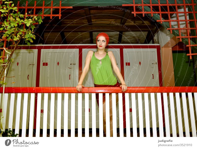 The girl with the beautiful red swim cap and green swimsuit is leaning on the railing of the ladies' changing room. A summer love. Girl Woman Swimwear