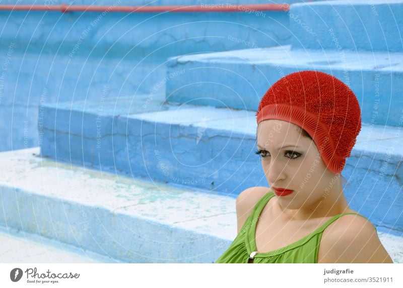 The girl with the beautiful red bathing cap and green swimsuit is sitting on the stairs of the empty non-swimmer's pool. A summer love. Girl Woman Swimwear