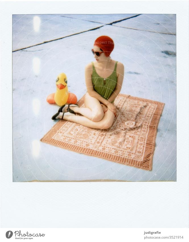 The girl with the beautiful red bathing cap and green swimsuit is sitting on a blanket with her rubber duck. A summer love. Girl Woman Swimwear Bathing cap