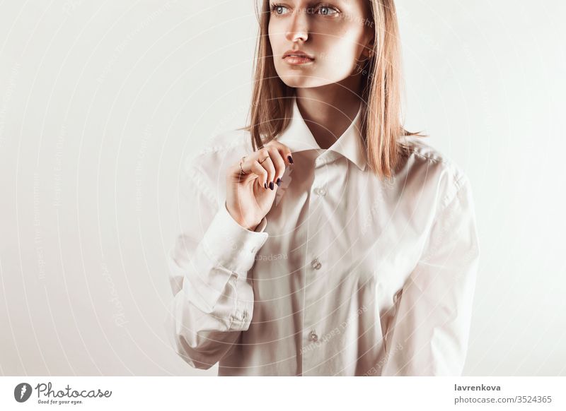 Portrait of young adult woman holding collar of white shirt with her hand, selective focus look clean skin natural makeup manicure rings jewelry studio bracelet