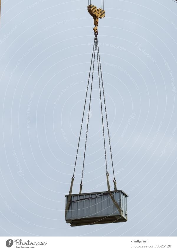 Grey metal container hangs high in the air on the hook of a construction crane Container Crane Safety lashed tethered Tall Above Steel cables Metal Sky