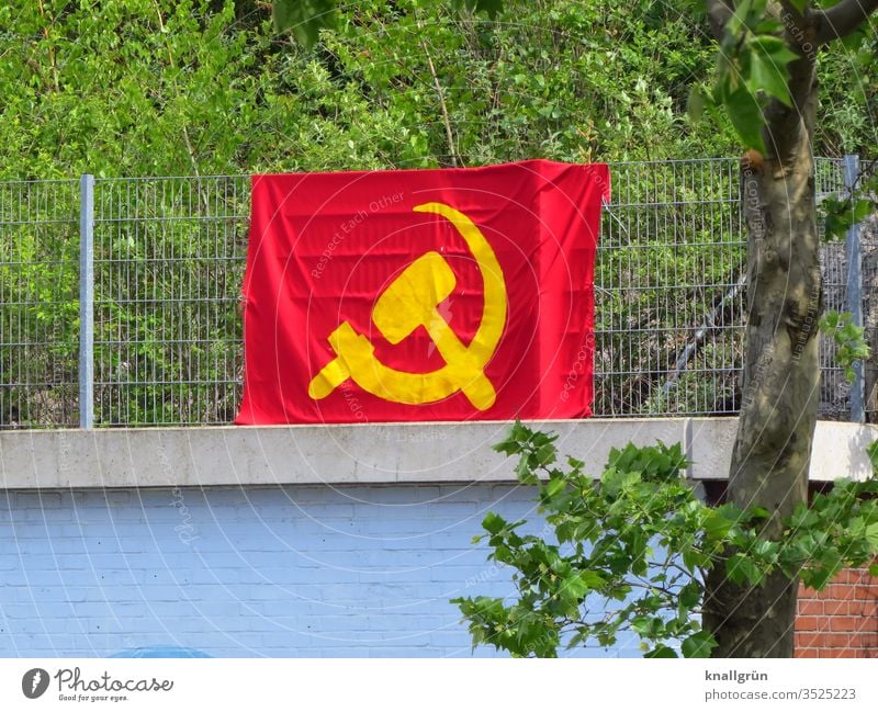 Large hammer and sickle flag attached to a metal fence above a wall Soviet Union Flag Hammer Red Yellow Communism Politics and state Symbols and metaphors