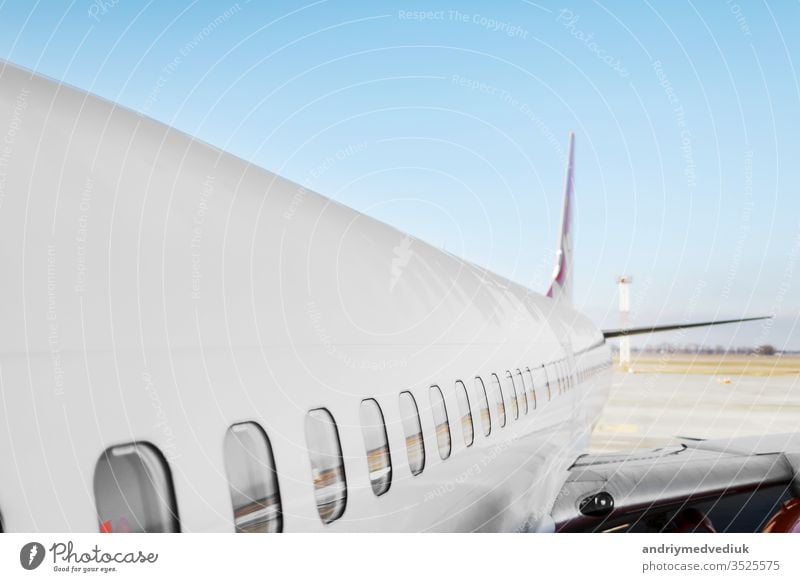 Aircraft porthole - side window airplain. White heavy passenger jet engine airplane on runway at airport against blue sky aviation transportation theme background.