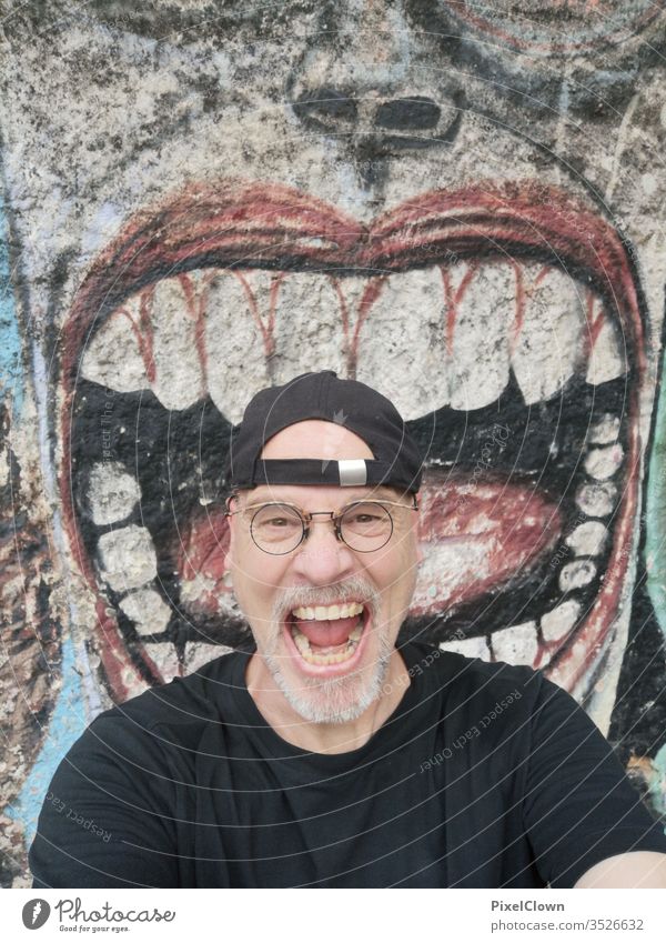 A screaming man in front of a graffiti Man Adults Human being Facial hair Head Masculine Eyeglasses Face Looking into the camera Graffiti