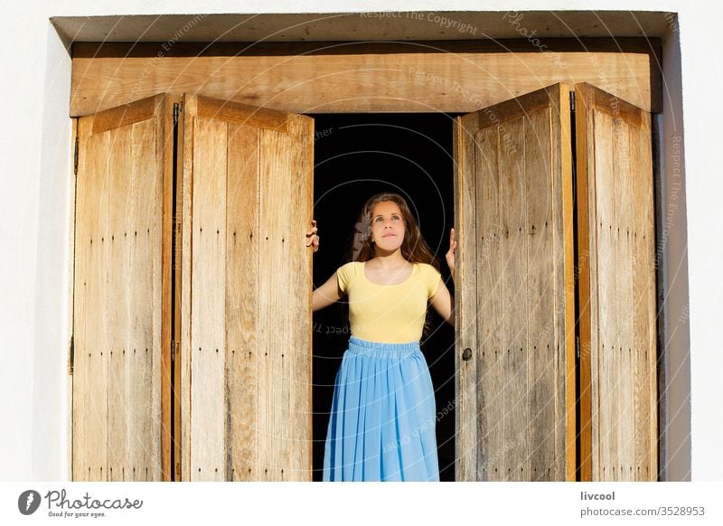 woman leaning out the door wanting to go outside during the quarantine by the covid-19 gate access entrance nostalgically waiting to get out wooden door