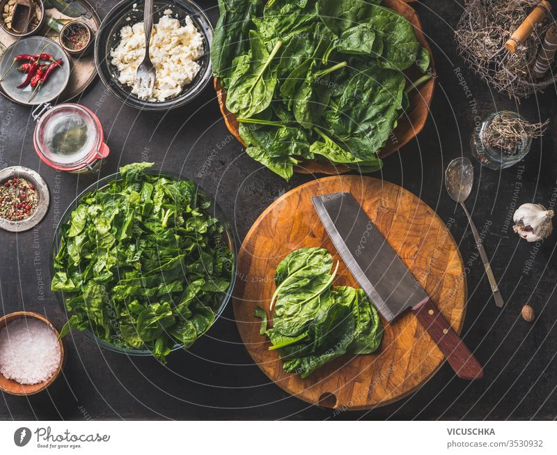Cooking preparation of delicious vegetarian spinach dish. Cutting board with knife on rustic kitchen background.  Healthy ingredients . Top view.