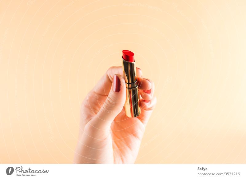 Female hand holding red lipstick on light orange glamour beauty female fashion color woman beautiful makeup closeup accessory nails personal girl fingers object