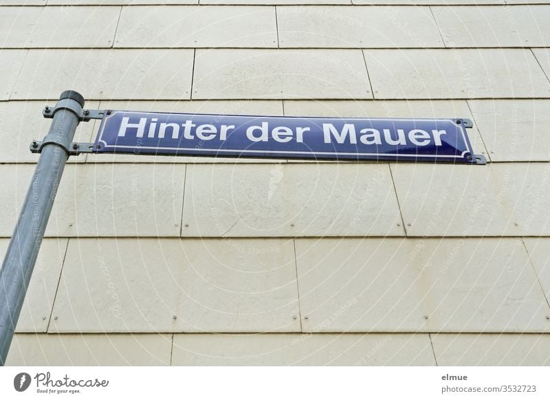 blue street sign "Hinter der Mauer" in front of a grey facade behind the wall Facade street name Blue Gray Clue signage Wall (building) Signs and labeling