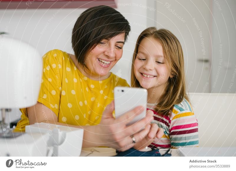 Happy seamstress taking selfie with daughter mother smartphone workshop tailor smile home together woman girl table cheerful adult child happy dressmaker