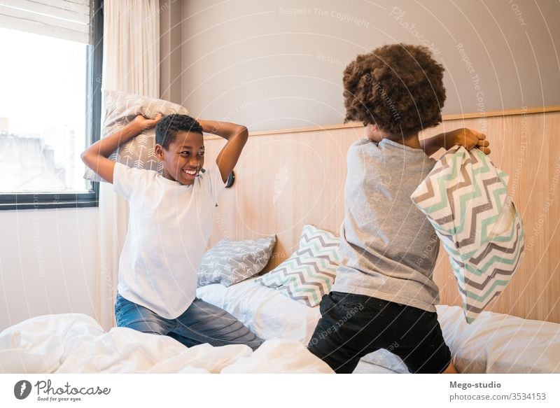Two brothers playing with pillows at home. kids together happy bedroom excited portrait positive active pillow fight adorable lifestyle black happiness