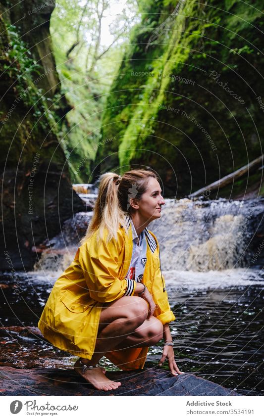 Cheerful female tourist crouching near waterfall and green mountain nature explore happy woman idyllic wanderlust paradise vacation cascade recreation harmony