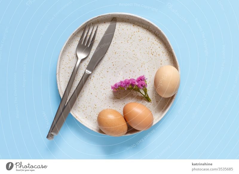Plate, eggs,flower, fork and knife over light blue background EASTER plate top view concept flat lay above celebration minimal negative space design festive