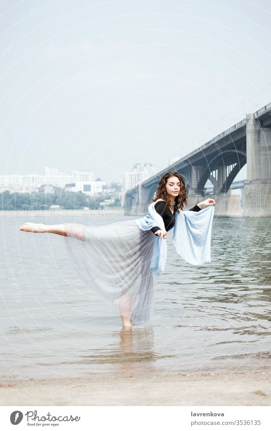 Young adult white female woman on a beach doing arabesque in the water, selective focus dancer movement beautiful aesthetic lifestyle dress nature sea