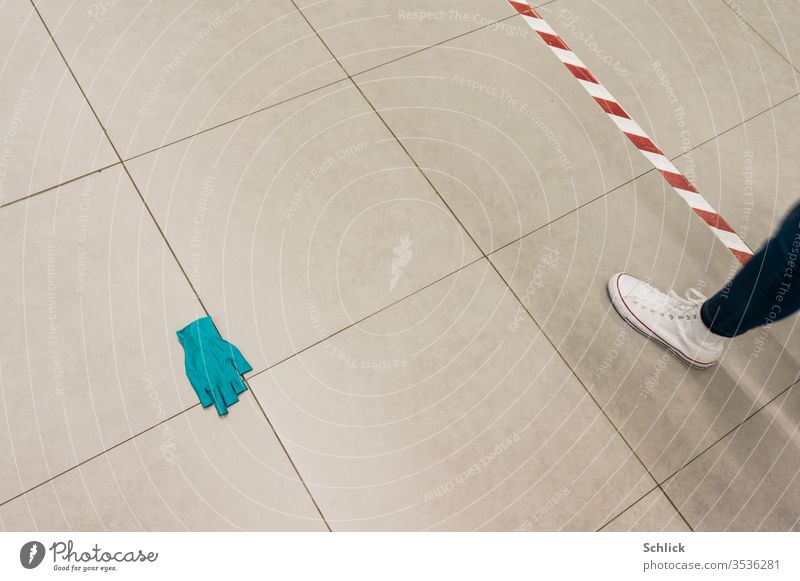 Coronakrise tiled floor with thrown away disposable glove Distance marker and leg of a passer-by corona crisis Ground tiles Lie Throw away distance marking