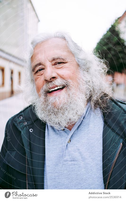 Cheerful old man with grey hair and long beard looking at camera cheerful happy senior traveler wisdom street portrait city pensioner town trip glad joy holiday