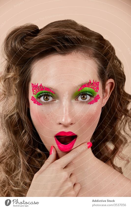 Amazed woman with bright makeup colorful amazed concept style rub chin mouth opened model young female appearance astonish surprise vivid vibrant trendy gesture