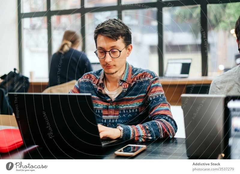 Focused worker using laptop in office man typing intelligent workplace professional workday smartphone project eyeglasses casual desk computer employee internet