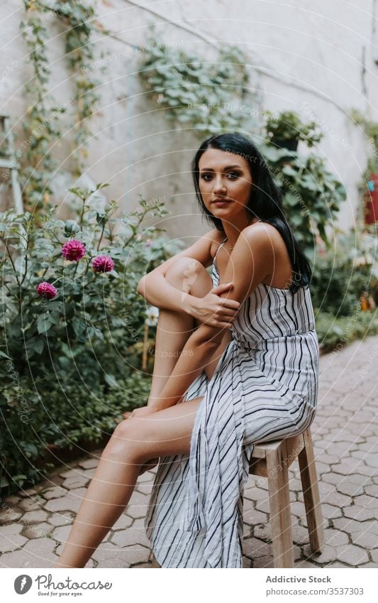 Young woman sitting on stool in garden old pavement style dress barefoot rest female path plant relax serene tranquil peaceful harmony calm summer idyllic flora