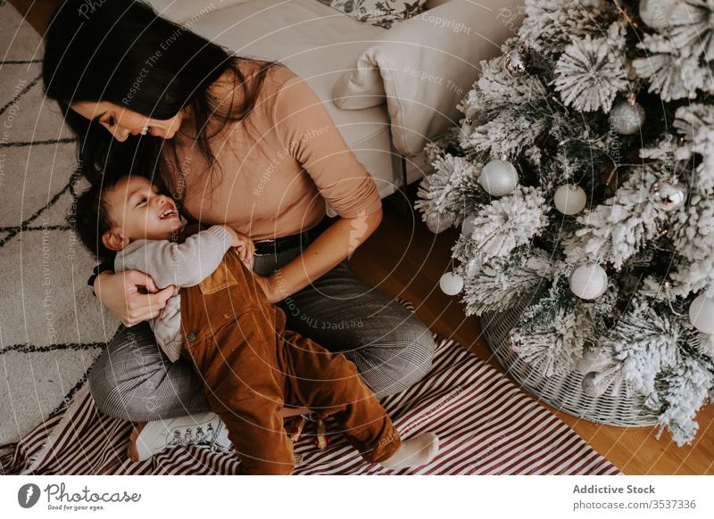 Cheerful loving mother hugging little son sitting on floor near Christmas tree cuddle christmas home playful cozy holiday smile child together kid parent