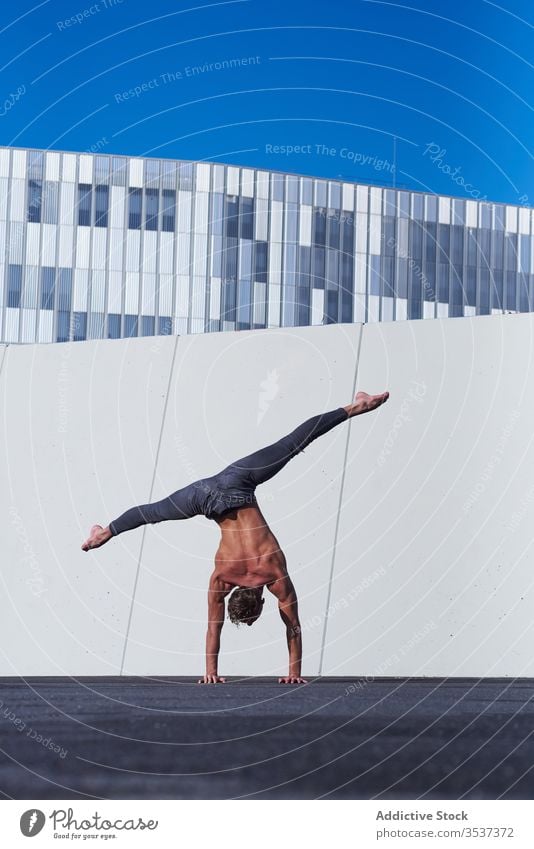 Male acrobat doing handstand on rooftop shirtless man urban upside down distant exercise stretch balance muscular perform strong modern architecture sportsman