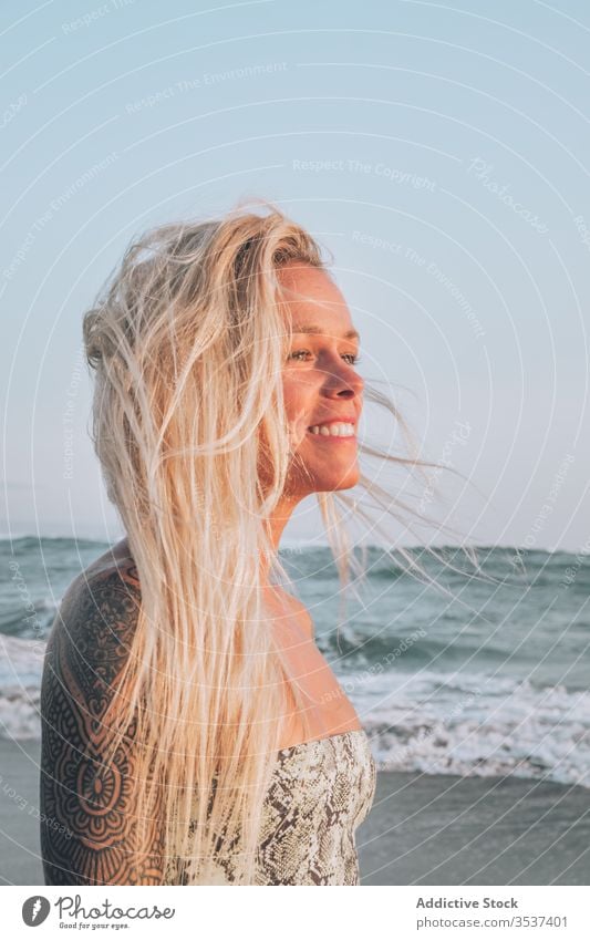 Smiling young blonde resting on seashore during sunny day woman beach shoulder tattoo summer sand vacation ocean relax coast nature travel happy leisure seaside