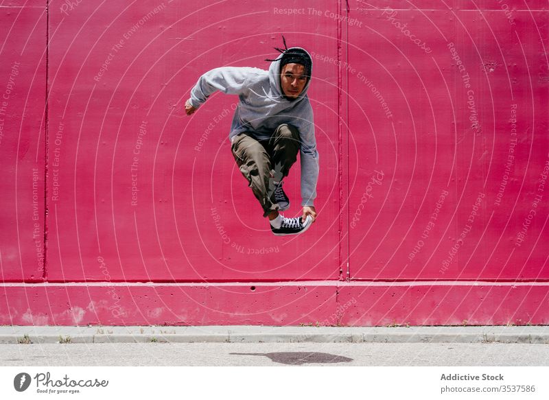Young hispanic men jumping near to a pink wall on the street urban dance lifestyle city posing standing colorful daylight mixed hat hip-hop cool modern male