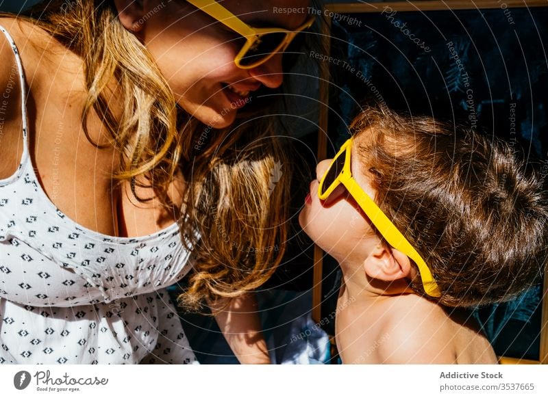 Positive mother playing with son in yellow sunglasses on sunny day home beach love dream together quarantine self isolation social distancing sunlight close