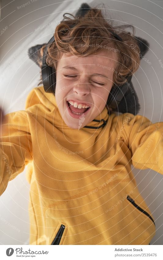 Satisfied child in headphones lying on table and enjoying music in light modern room boy chill listen home happy song music lover relax playlist lounge audio