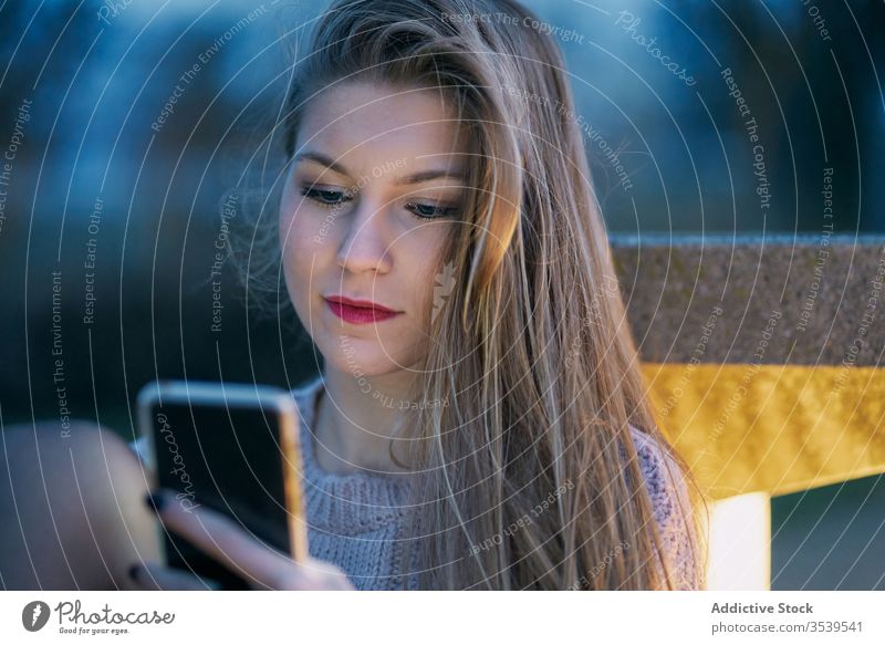 young girl who uses her cell phone at night leaning bench browse email reading sending skyscrapers check down internet message over seat smart sms typing