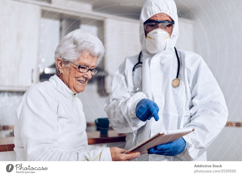 Doctor explaining medical information to senior patient at home during coronavirus quarantine doctor care tablet show point prescription practitioner