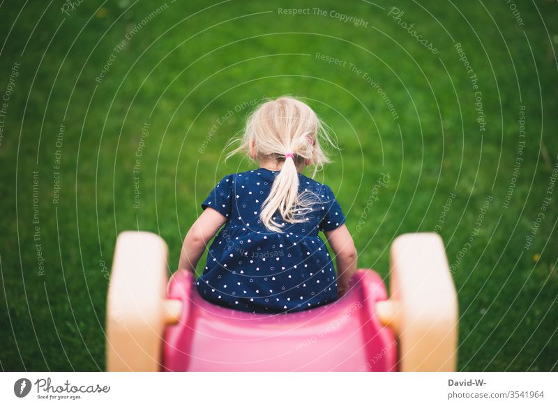 A Little Girl Sliding Down A Green Slide At The Playground. by