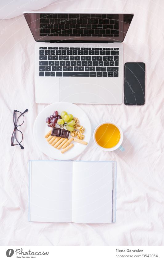 Flat lay. Tea at home in her bed, checking her laptop, reading a book and having breakfast. Top view flat lay books snack cozy indoors comfort comfortable